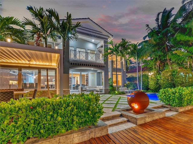 back house at dusk with a balcony and a patio