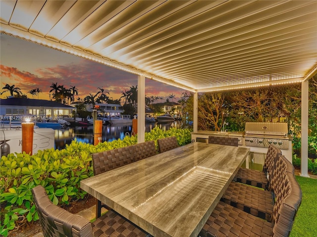 patio terrace at dusk featuring area for grilling and a water view