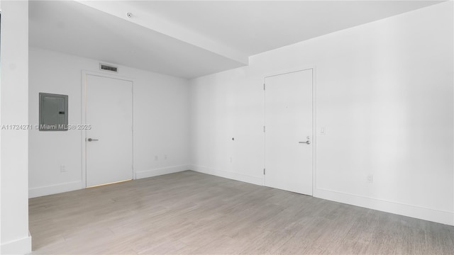 spare room with electric panel and light hardwood / wood-style flooring