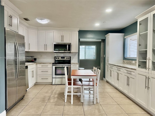 kitchen featuring backsplash, stainless steel appliances, light stone counters, and white cabinetry