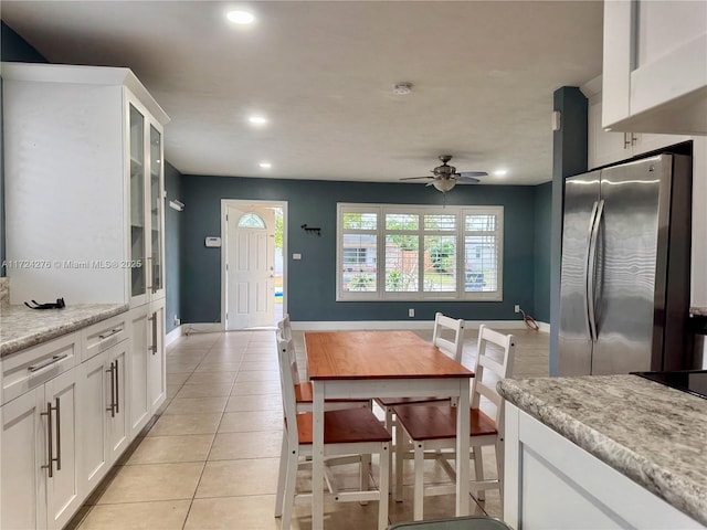 kitchen with white cabinets, light tile patterned flooring, stainless steel refrigerator, and light stone counters