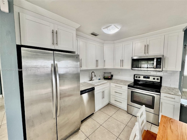 kitchen with sink, light tile patterned floors, light stone counters, white cabinets, and appliances with stainless steel finishes