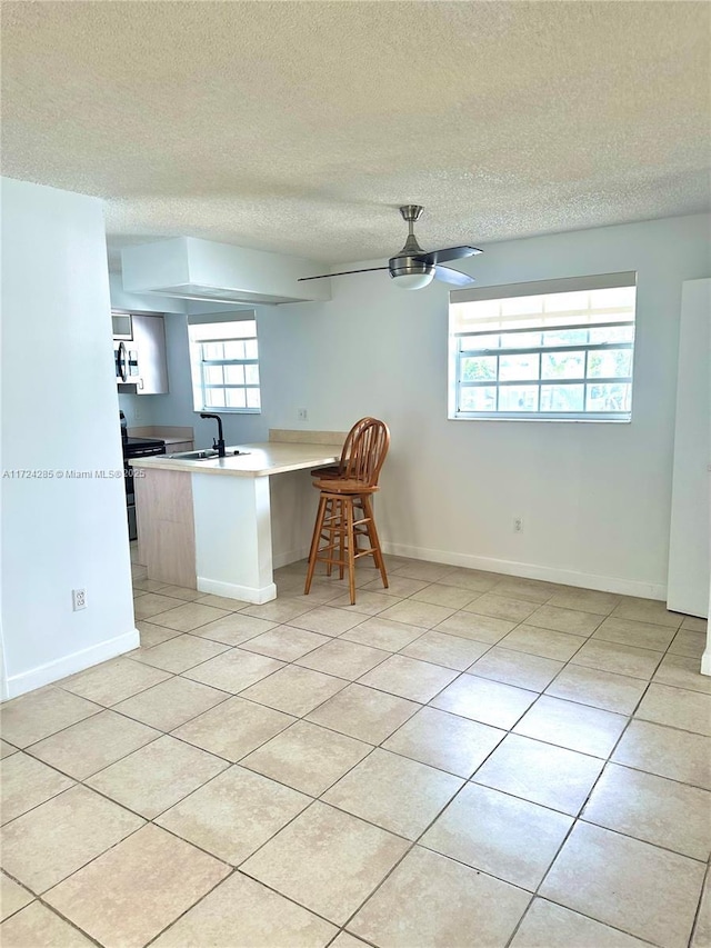 kitchen featuring sink, ceiling fan, stainless steel range with electric stovetop, a kitchen breakfast bar, and kitchen peninsula