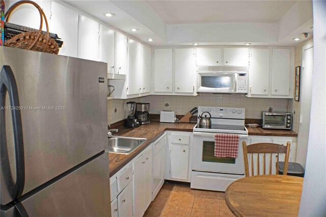 kitchen with sink, light tile patterned floors, backsplash, white appliances, and white cabinets