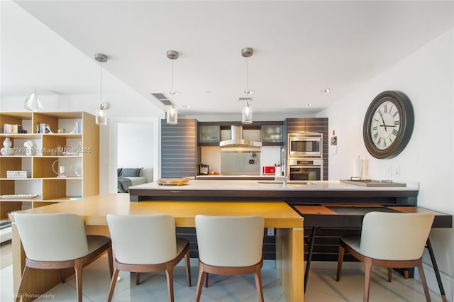 interior space featuring pendant lighting, wall chimney range hood, and appliances with stainless steel finishes