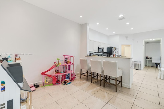 kitchen with a breakfast bar, white cabinets, light tile patterned floors, kitchen peninsula, and stainless steel appliances