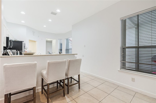 kitchen featuring light tile patterned floors, white cabinets, a kitchen bar, and kitchen peninsula