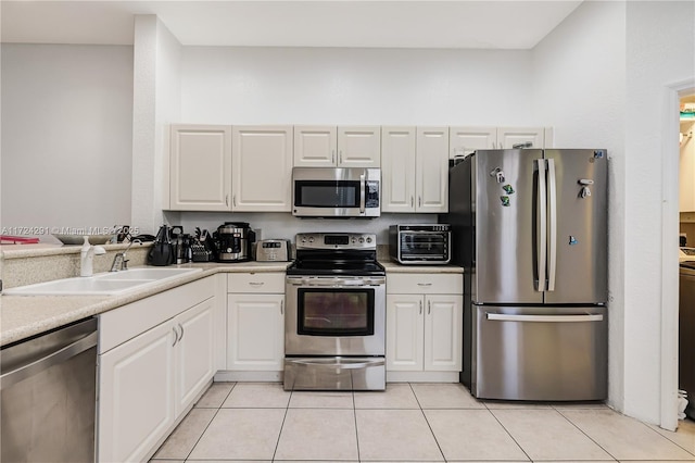 kitchen with light tile patterned flooring, appliances with stainless steel finishes, sink, and white cabinets