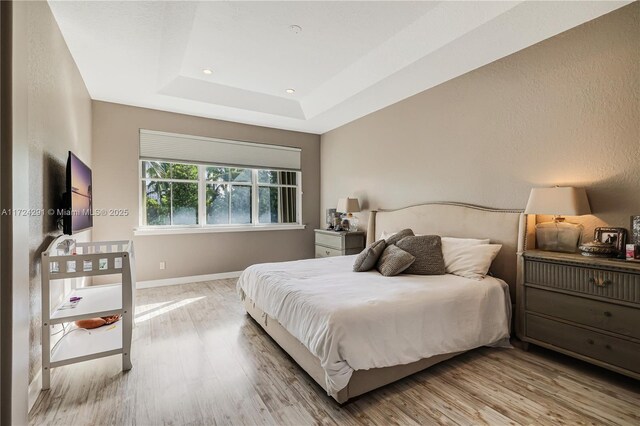 bedroom featuring a tray ceiling and light wood-type flooring