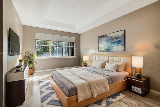 bedroom with a tray ceiling and light wood-type flooring