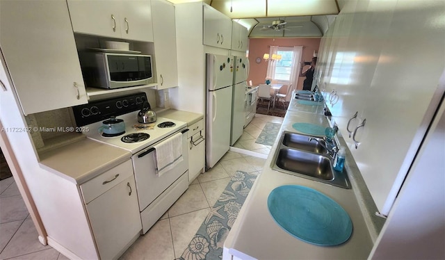 kitchen with white appliances, light tile patterned floors, ceiling fan with notable chandelier, white cabinets, and sink