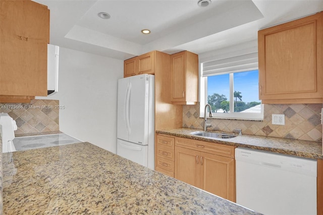 kitchen with a tray ceiling, white appliances, a sink, and light stone countertops