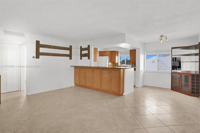 kitchen featuring light tile patterned floors, a peninsula, visible vents, freestanding refrigerator, and brown cabinets