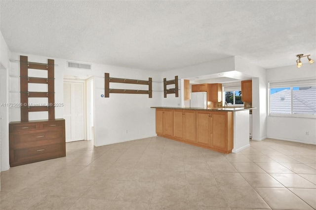 kitchen featuring brown cabinets, visible vents, freestanding refrigerator, a textured ceiling, and a peninsula