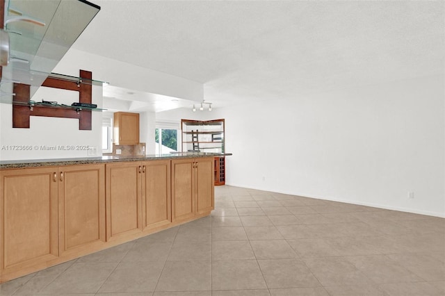 kitchen with light tile patterned floors, a peninsula, dark stone counters, and baseboards