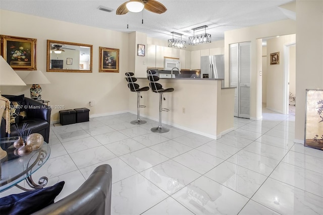 kitchen with dark countertops, white microwave, a peninsula, white cabinetry, and stainless steel refrigerator with ice dispenser