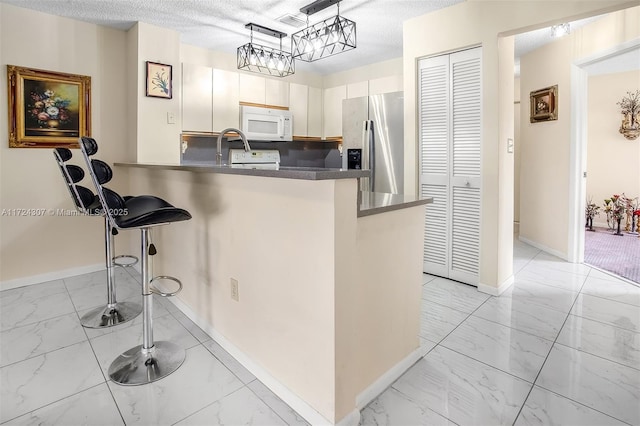 kitchen with white microwave, a peninsula, marble finish floor, dark countertops, and stainless steel fridge