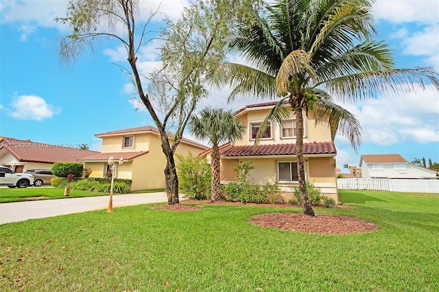 view of front of home with concrete driveway, a tiled roof, fence, a front lawn, and stucco siding