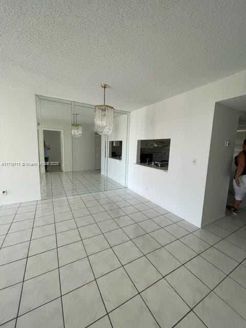 unfurnished room featuring a notable chandelier, a textured ceiling, and light tile patterned floors