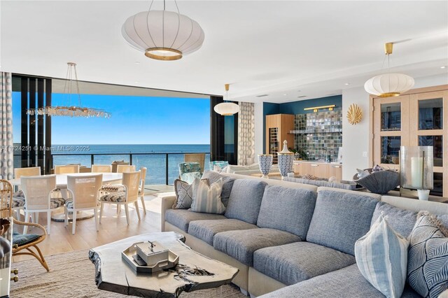 living room with an inviting chandelier, light wood-type flooring, expansive windows, and a water view