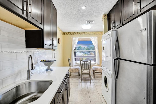 kitchen with stacked washer / drying machine, a textured ceiling, stainless steel fridge, sink, and dark brown cabinets