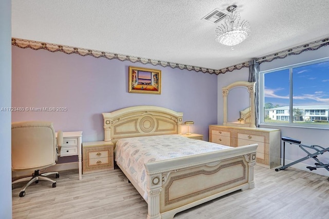 bedroom featuring a textured ceiling, a notable chandelier, and light hardwood / wood-style flooring