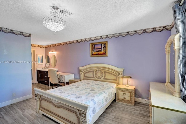 bedroom featuring ensuite bathroom, light wood-type flooring, a notable chandelier, and a textured ceiling