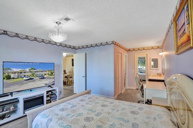 bedroom featuring a textured ceiling, light hardwood / wood-style flooring, and an inviting chandelier