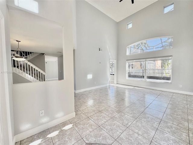 interior space with ceiling fan with notable chandelier, a towering ceiling, and light tile patterned flooring