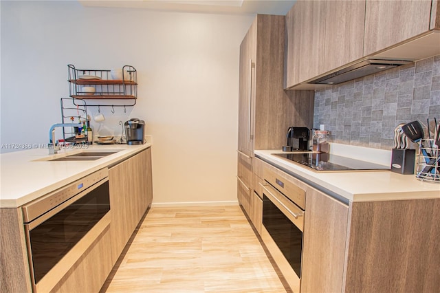 kitchen with stainless steel oven, black electric cooktop, sink, light brown cabinets, and light hardwood / wood-style floors