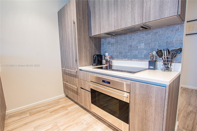 kitchen with black electric stovetop, tasteful backsplash, light hardwood / wood-style flooring, and stainless steel oven