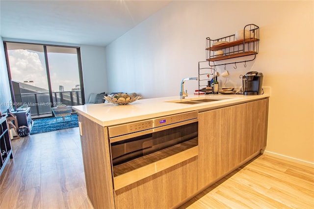 kitchen featuring kitchen peninsula, light wood-type flooring, sink, a wall of windows, and oven