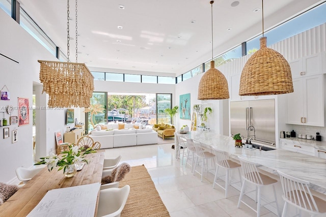 kitchen featuring sink, an inviting chandelier, built in fridge, light stone counters, and white cabinets