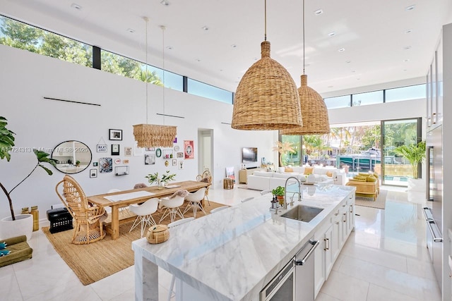 kitchen featuring white cabinets, sink, hanging light fixtures, a towering ceiling, and light stone counters