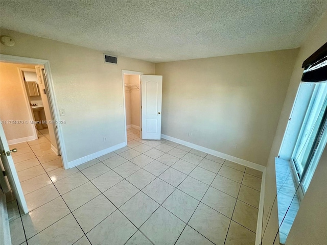 unfurnished bedroom with a spacious closet, a textured ceiling, light tile patterned floors, and a closet