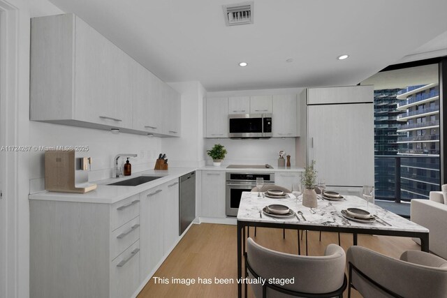 kitchen featuring sink, light hardwood / wood-style flooring, appliances with stainless steel finishes, white cabinetry, and a kitchen bar