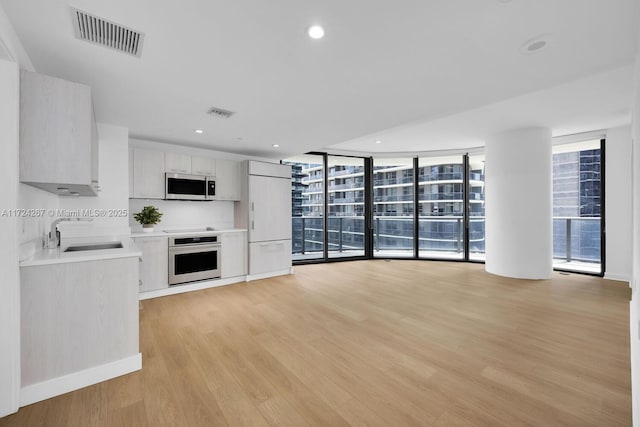 kitchen featuring white cabinets, sink, oven, and light wood-type flooring