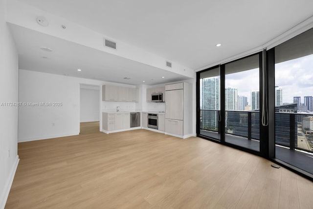 unfurnished living room with sink, a wall of windows, and light hardwood / wood-style floors