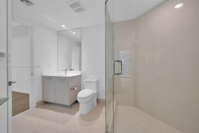 bathroom featuring vanity, tile patterned flooring, toilet, and a tile shower