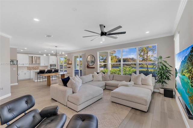 living room with ceiling fan with notable chandelier, light wood-type flooring, and ornamental molding