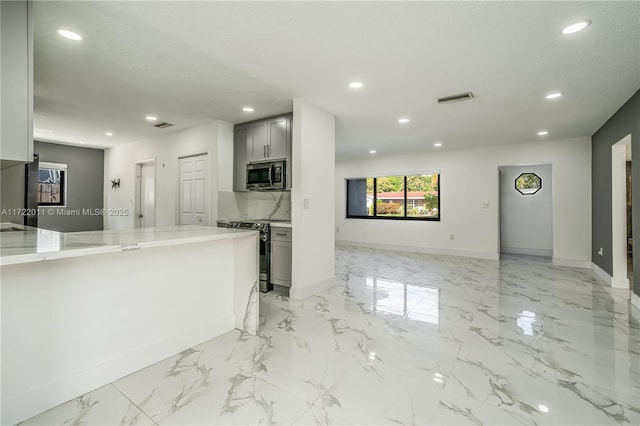 kitchen with gray cabinetry, light stone countertops, stainless steel appliances, and tasteful backsplash