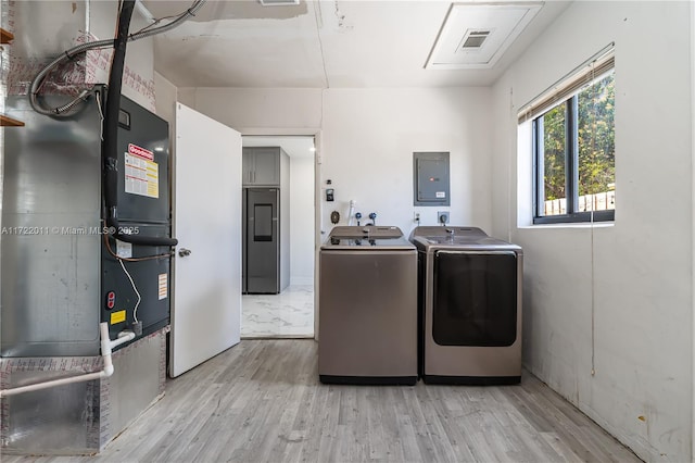 laundry room featuring heating unit, light hardwood / wood-style floors, electric panel, and washing machine and clothes dryer