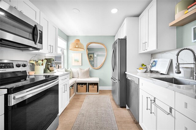 kitchen featuring sink, white cabinetry, appliances with stainless steel finishes, pendant lighting, and light stone countertops