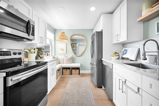 kitchen with tasteful backsplash, appliances with stainless steel finishes, light wood-style floors, white cabinets, and a sink