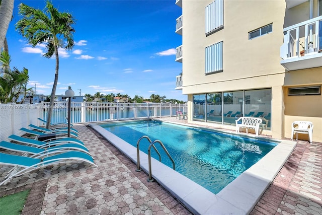 community pool with a water view, fence, and a patio