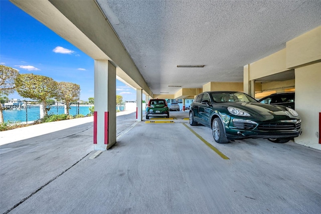 view of vehicle parking with a water view and fence