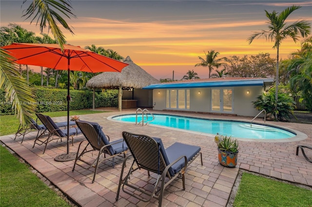 pool at dusk with french doors and a patio area