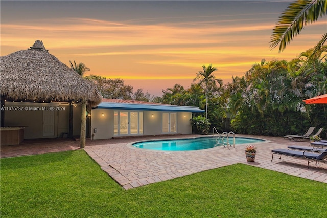 pool at dusk featuring a gazebo, a patio area, and a lawn