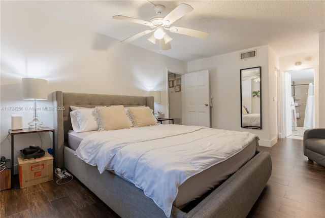 bedroom with a textured ceiling, dark hardwood / wood-style flooring, ceiling fan, and connected bathroom