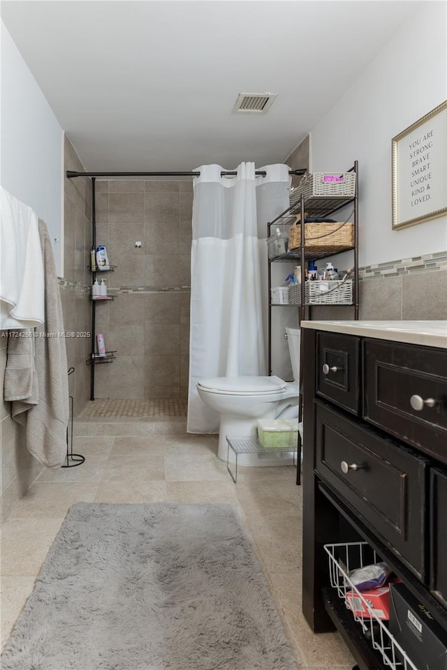 bathroom with curtained shower, vanity, tile walls, and toilet